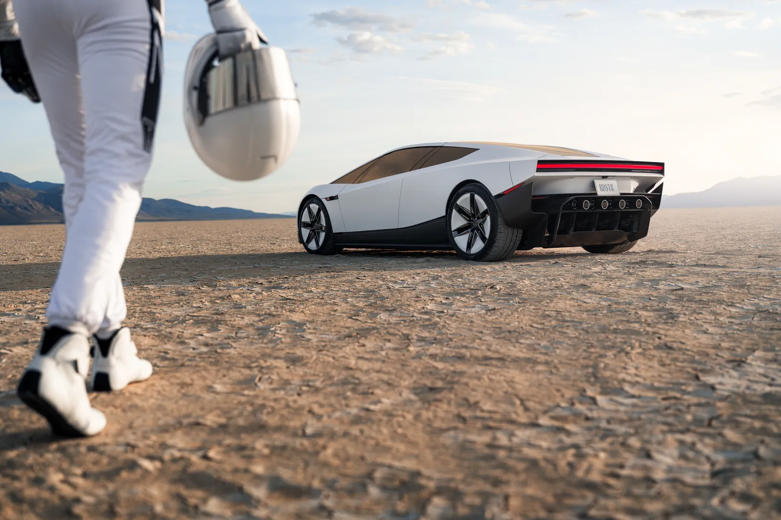 An astronaut walks across a dry lakebed at dawn toward a white Roadster.