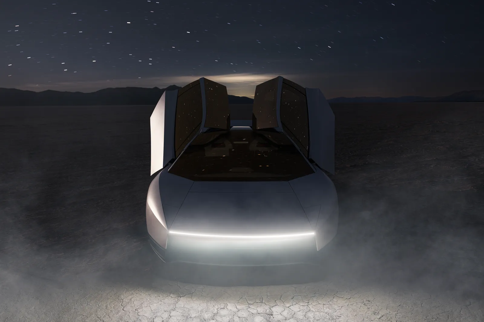 Roadster head-on at night, canopy raised, its concealed headlights reading as one thin light bar.