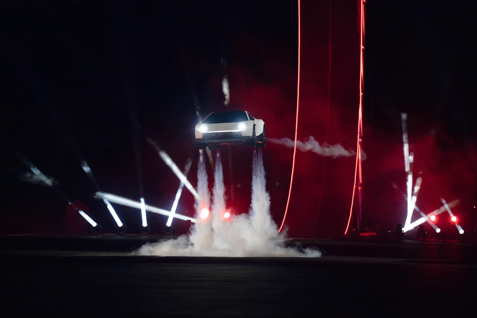 Roadster hovering on thrusters between red stage lights and searchlights.